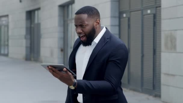 Geschäftsmann schaut auf dem Tablet-Bildschirm auf der Straße. Afro mann mit kissen outdoor — Stockvideo
