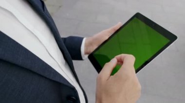 İş adamı açık hava tabletinde internete göz atıyor. Erkek eller pedde yazıyor.