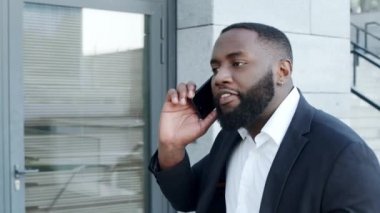 Afro iş adamı şehirde akıllı telefondan tartışıyor. Erkek yönetici telefonda konuşuyor.