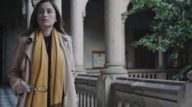 Öğrenci sütun koridorunda yürüyor. İş kadını dışarıda gözlük takıyor.