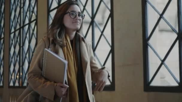 Estudiante caminando por el pasillo de la universidad. Woamn sosteniendo el cuaderno en la mano — Vídeos de Stock