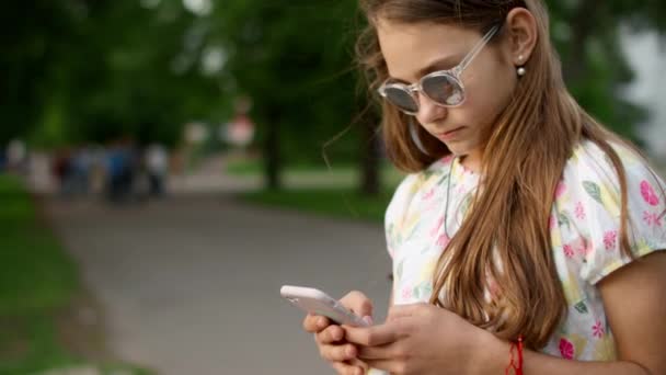 Menina alegre jogando jogos no telefone no parque. Menina brincalhão usando smartphone — Vídeo de Stock