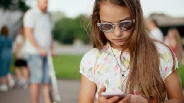 Закрыть серьезную девочку-подростка, просматривающую смартфон в летнем парке — стоковое видео