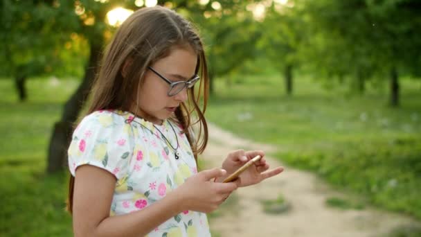 Ernstes Mädchen, das Spiele am Telefon spielt. Konzentriertes Mädchen steht im Sommerpark — Stockvideo