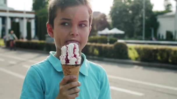 Zamknij tego słodkiego chłopca jedzącego lody. Zrelaksowane dziecko spacerujące w parku rozrywki — Wideo stockowe