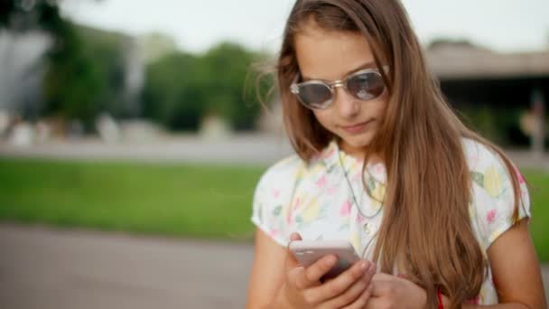 Улыбающаяся девушка играет в игры на улице на мобильном телефоне. Девушка стоящая в парке — стоковое видео