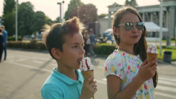 Roztomilá sestra a bratr jedí zmrzlinu. Usmívající se děti procházející se v zábavním parku