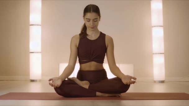Mujer sentada en loto posando en la alfombra interior. Entrenador practicando yoga en estudio — Vídeos de Stock