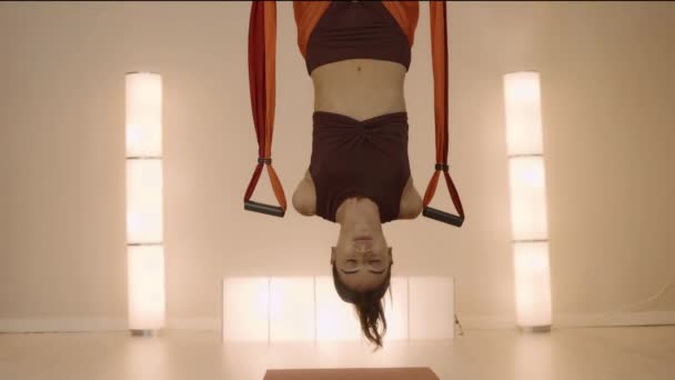 Kvinnan hänger upp och ner i hängmattan i studion. Flicka som utövar antigravitationyoga — Stockvideo