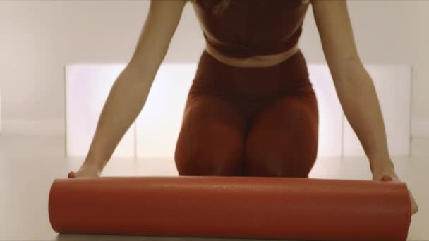 Mulher rolando tapete de ioga antes do treinamento. Menina preparando equipamentos para ioga — Vídeo de Stock