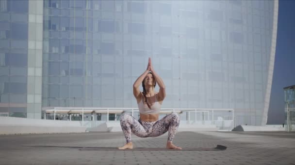 Mujer haciendo guirnaldas posando en esterilla de yoga en la calle. Entrenador de yoga haciendo ejercicio afuera — Vídeos de Stock