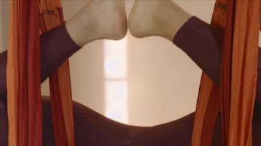 Stüdyoda ters kelebek pozu veren bir kadın. Antrenör uçuş yogası yapıyor