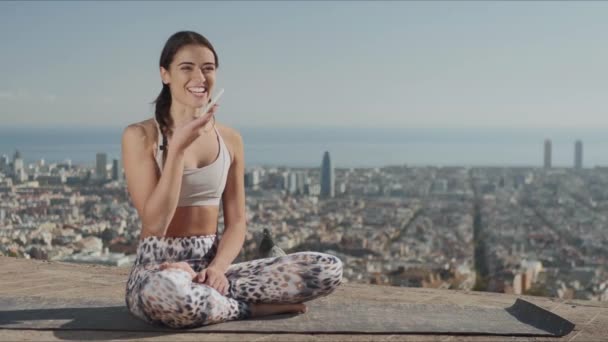Yoga mujer grabando mensaje de voz en smartphone con vista a la ciudad de Barcelona — Vídeos de Stock