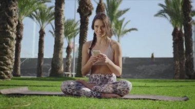 Lotus 'ta oturan kadın akıllı telefonuyla poz veriyor. Parkta cep telefonu kullanan kız