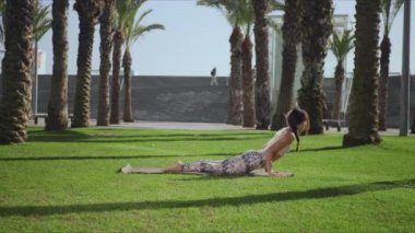 Yoga eğitmeni parkta kobra pozu veriyor. Yeşil çimenler üzerinde yoga yapan kadın.