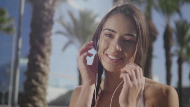 Mujer poniéndose auriculares en el parque. Chica escuchando música en auriculares al aire libre — Vídeos de Stock