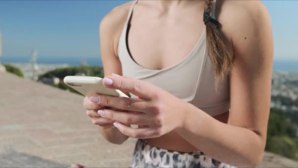 Sporcu kadın açık hava antrenmanından sonra akıllı telefon kullanıyor. Telefonla yazı yazan kadın elleri — Stok video