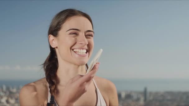 Portret van een lachende vrouw die een voicemail opneemt op een mobiele telefoon op straat — Stockvideo