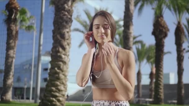 Chica en forma sentada en pose de loto en el parque. Mujer en auriculares meditando al aire libre — Vídeos de Stock