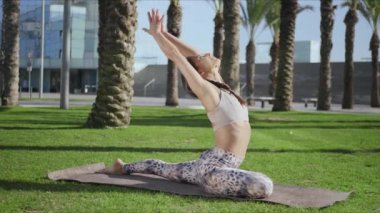 Parkta esneme hareketleri yapan atletik kız. Yeşil çimenler üzerinde yoga egzersizleri yapan bir kadın.