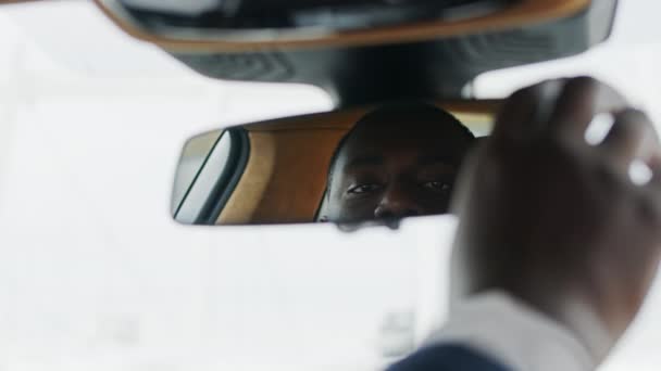 Primer plano ajustando el espejo retrovisor en el coche. Hombre africano sentado frente al coche — Vídeos de Stock