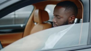 Yakından bir iş adamı kameraya bakıyor. Afrikalı adam lüks bir arabada gülümsüyor.