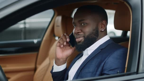 Крупный бизнесмен говорит по телефону в новой машине. Африканский мужчина сидит у роскошного автомобиля — стоковое видео
