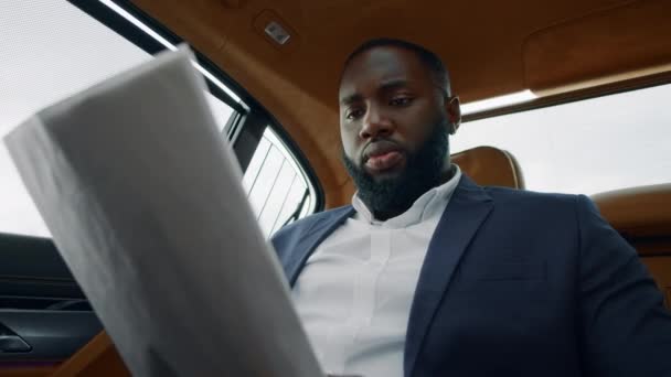 Nahaufnahme afrikanischer Mann beim Lesen von Dokumenten in einem Luxusauto. Geschäftsmann wirft mit Papier — Stockvideo