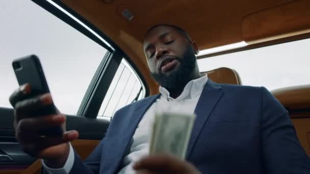 Nahaufnahme eines Mannes, der am Auto ein Video anruft. Afro-Mann schüttelt Geld auf Rücksitz — Stockvideo