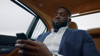 Arabada cep telefonunu daktilo eden yakın çekim adamı. Afro işadamı akıllı telefondan konuşuyor