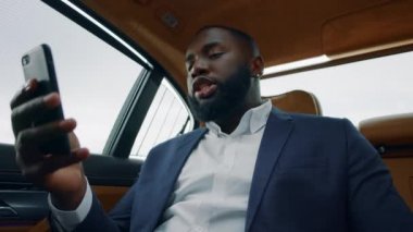 Yakından Afrikalı bir adam arabada video görüşmesi yapıyor. İş adamı arabada telefonla konuşuyor.