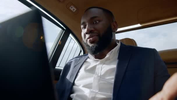 Gros plan en colère homme d'affaires africain argumentant sur appel vidéo sur ordinateur portable à la voiture. — Video