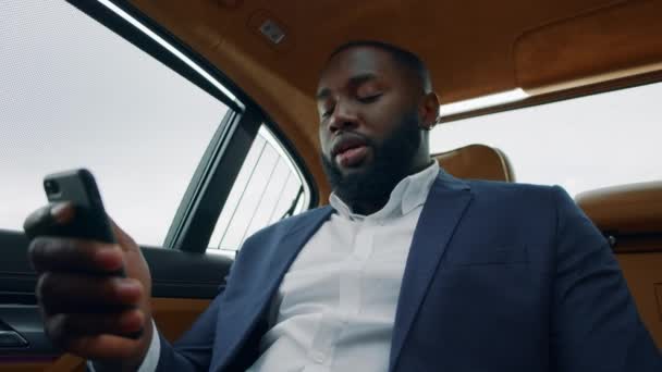 Крупним планом африканський чоловік тримає телефон на задньому сидінні. Чоловік має відеодзвінок на машині — стокове відео