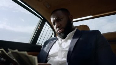 Yakından bir iş adamı arabada dolar sayıyor. Arabada paralı bir adam oturuyor.