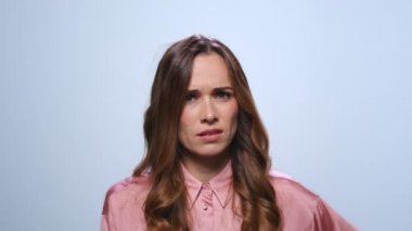 Mavi arka planda el kol hareketi yapan hoşnutsuz iş kadını. Kameraya bakan kadın.