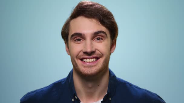Positiver Mann winkt kopfschüttelnd in die Kamera. Mann lächelt auf blauem Hintergrund — Stockvideo