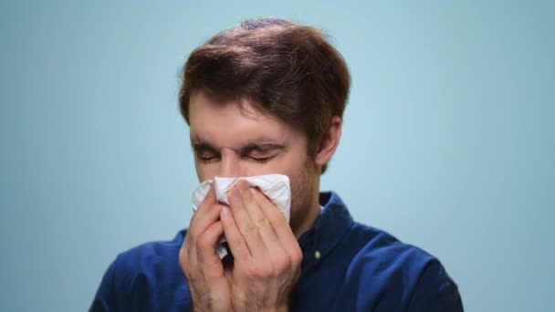 Sick man sneezing in studio. Ill man using napkin on blue background — Stock Video