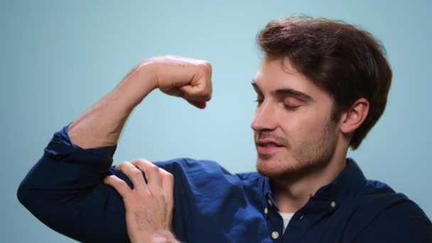 Young man showing biceps on blue background. Strong man posing at camera — Stock Video