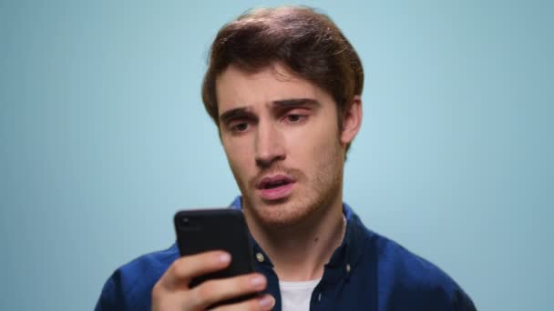 Hombre molesto leyendo malas noticias en el teléfono inteligente. Chico triste usando el teléfono en el estudio — Vídeo de stock