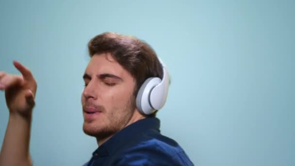 Man dancing in headphones on blue background. Guy listening music in earphones — Stock Video