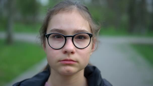 Портрет серьёзной девушки в парке. Девушка-подросток смотрит в камеру на улице. — стоковое видео