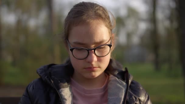 Портрет серьезной девушки сидящей в парке. Девочке-подростку грустно на улице.. — стоковое видео