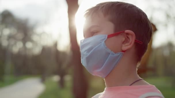 En seriös kille som står i medicinsk mask utomhus. Tonårspojken tar bort masken — Stockvideo