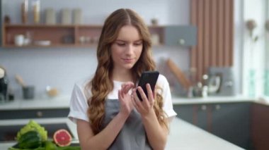 Mutfakta telefonu kullanan güzel bir kadın. Mutlu ev hanımı evde yemek hazırlıyor.