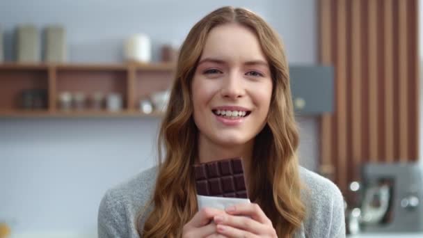 Красивая девушка пробует шоколад в помещении. Улыбающаяся женщина наслаждается тёмным шоколадом — стоковое видео