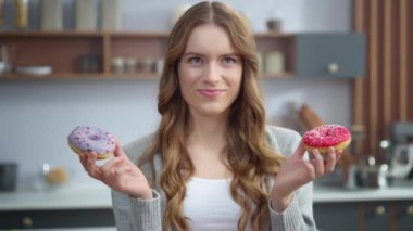 Gülümseyen kadın evde iki donut arasında seçim yapıyor. Kız pastalarla eğleniyor..