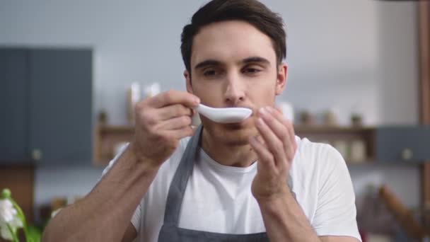 Retrato del hombre cocinero degustando sopa fresca en la cocina casera. Chef masculino cocina comida — Vídeos de Stock