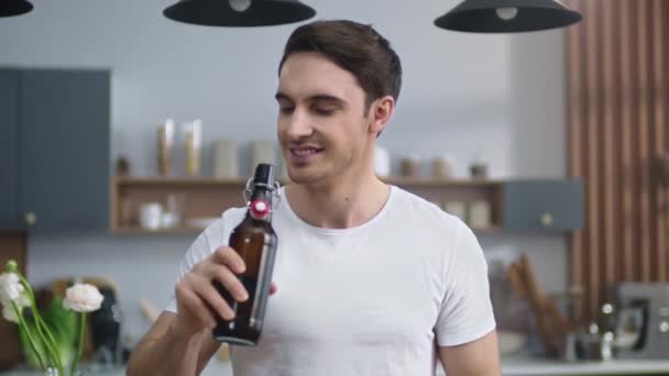 Πορτρέτο του χαρούμενου άντρα που ανοίγει μπύρα στην κουζίνα του σπιτιού. Νεαρός απολαμβάνει αλκοόλ — Αρχείο Βίντεο