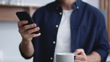 Bilinmeyen adam mutfakta akıllı telefondan yazı yazıyor. Çay içen tanınmamış bir adam..