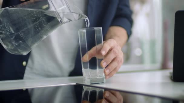 Closeup male hands pouring water into glass from jug at kitchen background. — Stock Video